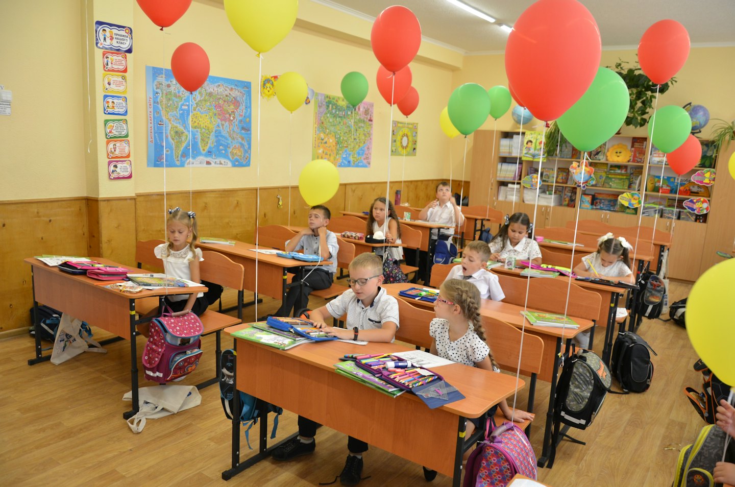 Kinder sitzen an Holztischen in einem dekorierten Klassenzimmer.