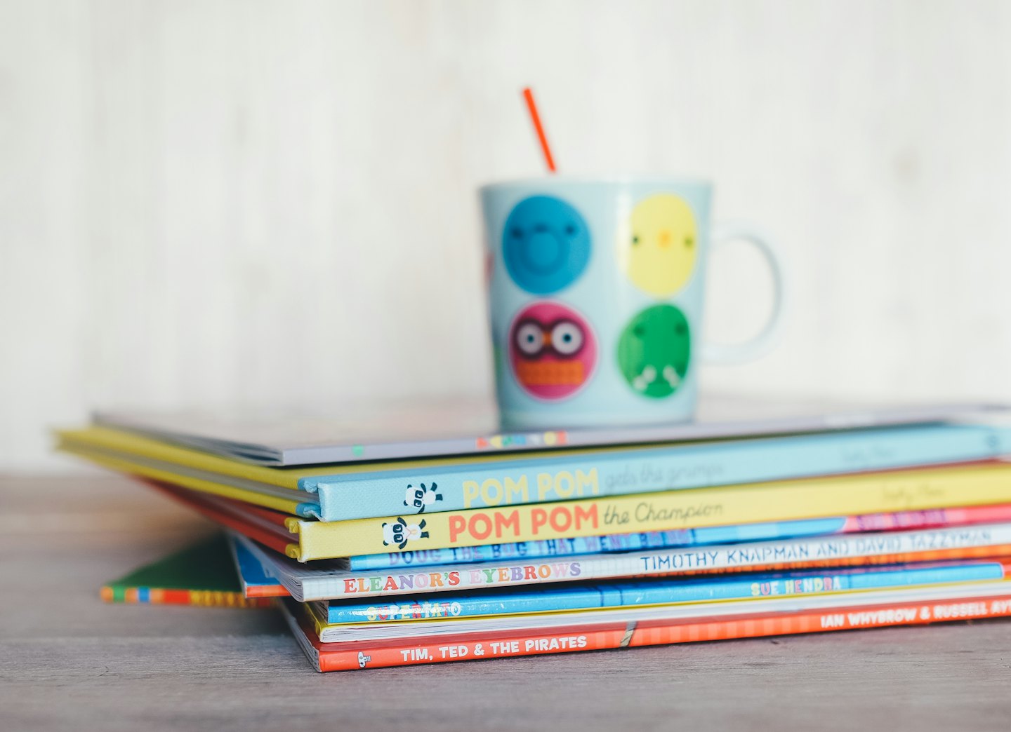Bunte Kinderbücher mit einer Tasse und einem Strohhalm obendrauf.