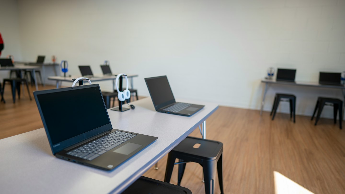 Leerer moderner Klassenraum mit Laptops und Kopfhörern auf den Schreibtischen.