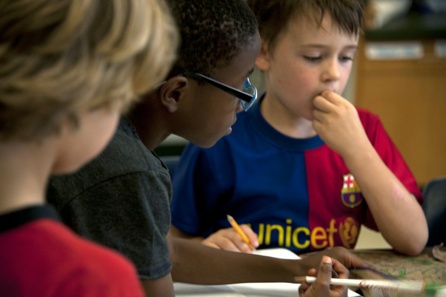 Drei kleine Kinder arbeiten gemeinsam mit Bleistiften an einem Tisch.